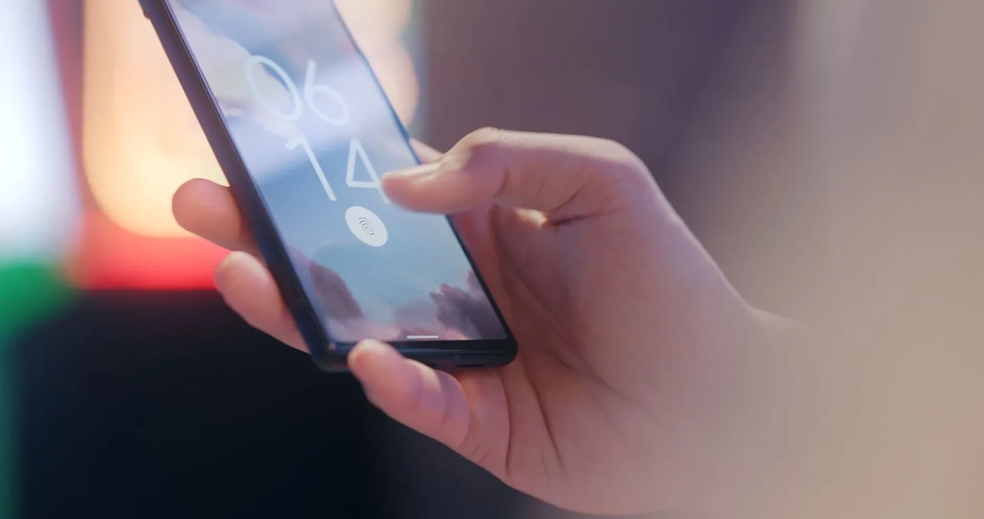 時刻と指紋のアイコンが表示されたスマートフォンのロック画面を片手で持っている