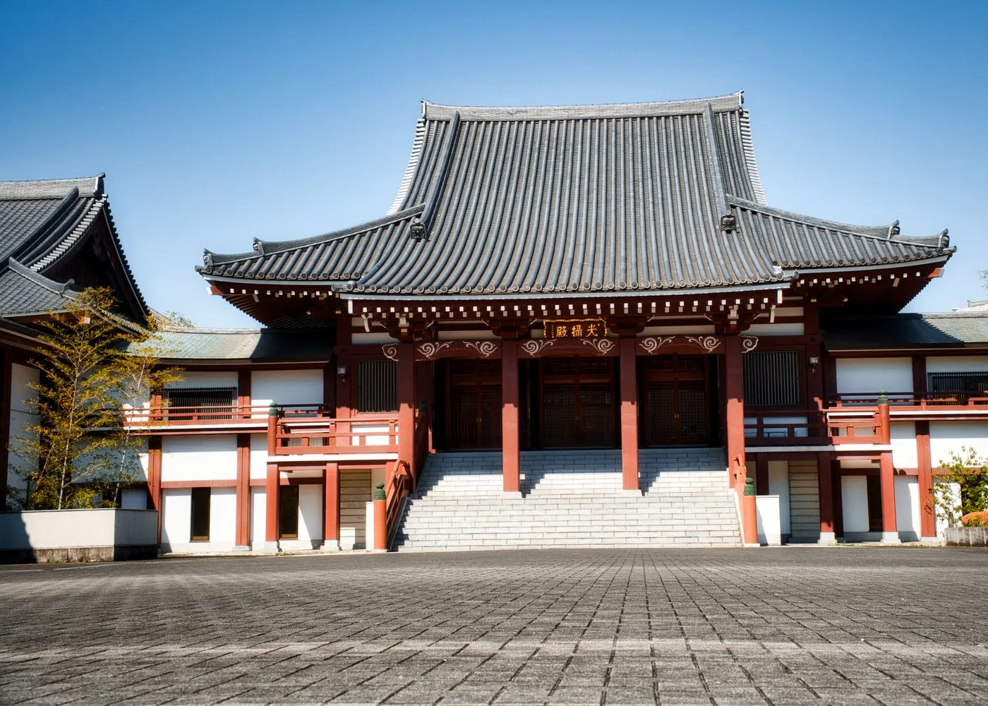 寄棟の瓦屋根と朱塗りの柱を持つ日本の寺院建築。正面に石段が伸びている