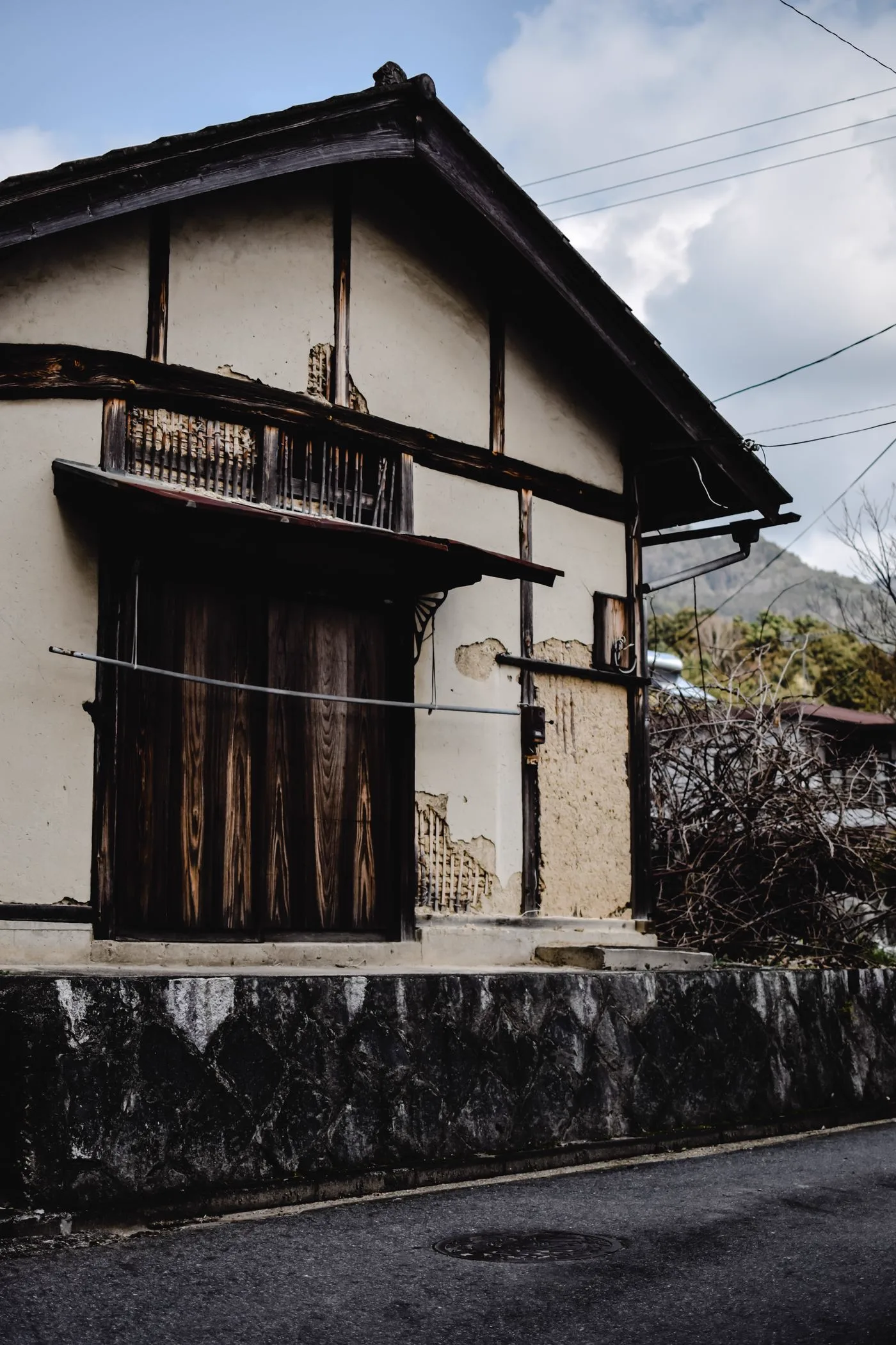 漆喰と焼き板の外壁に木の引き戸がある二階建ての日本家屋と、手前の石垣