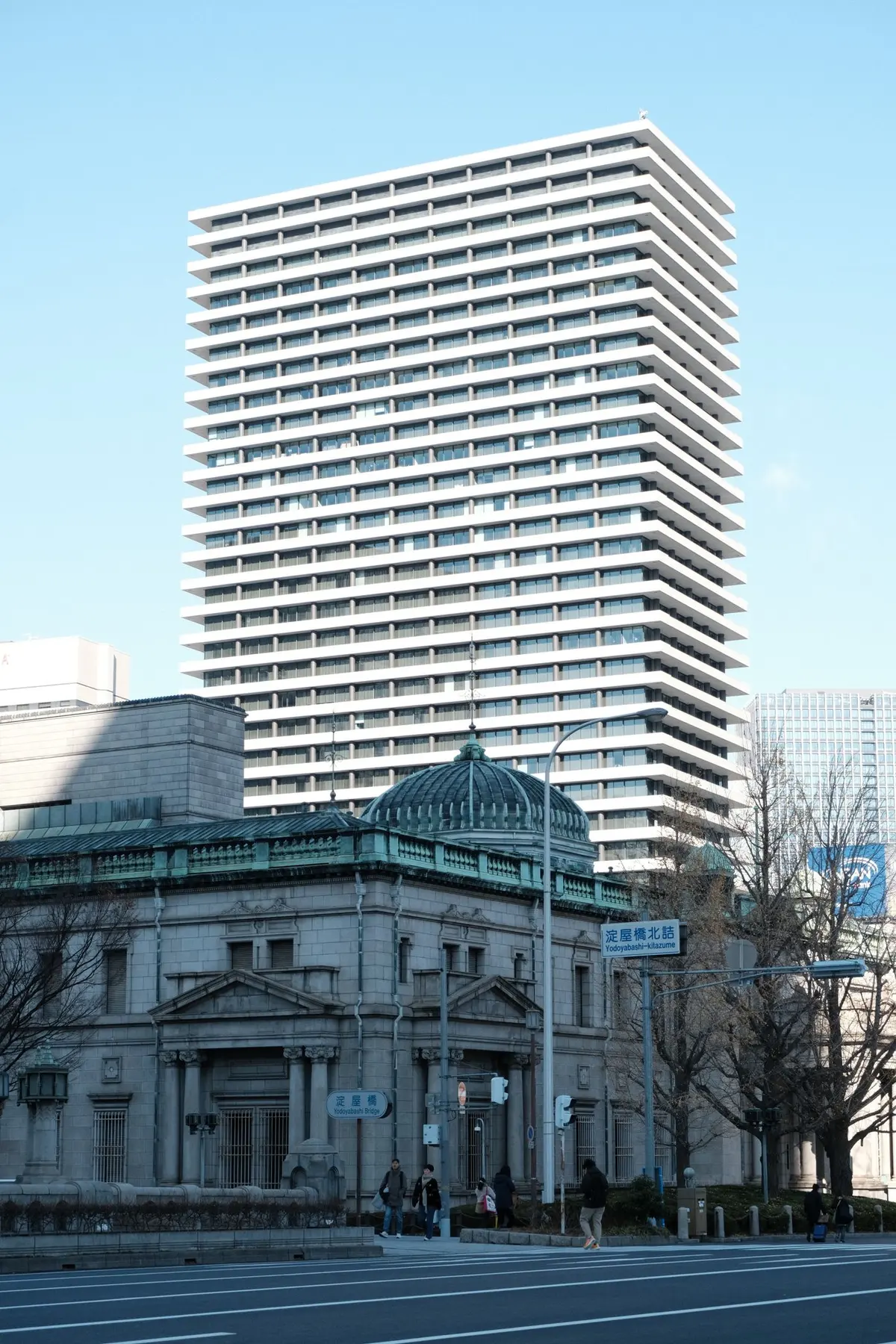 川沿いの交差点に立つ高層の庁舎と、その手前にあるドーム屋根の石造建築
