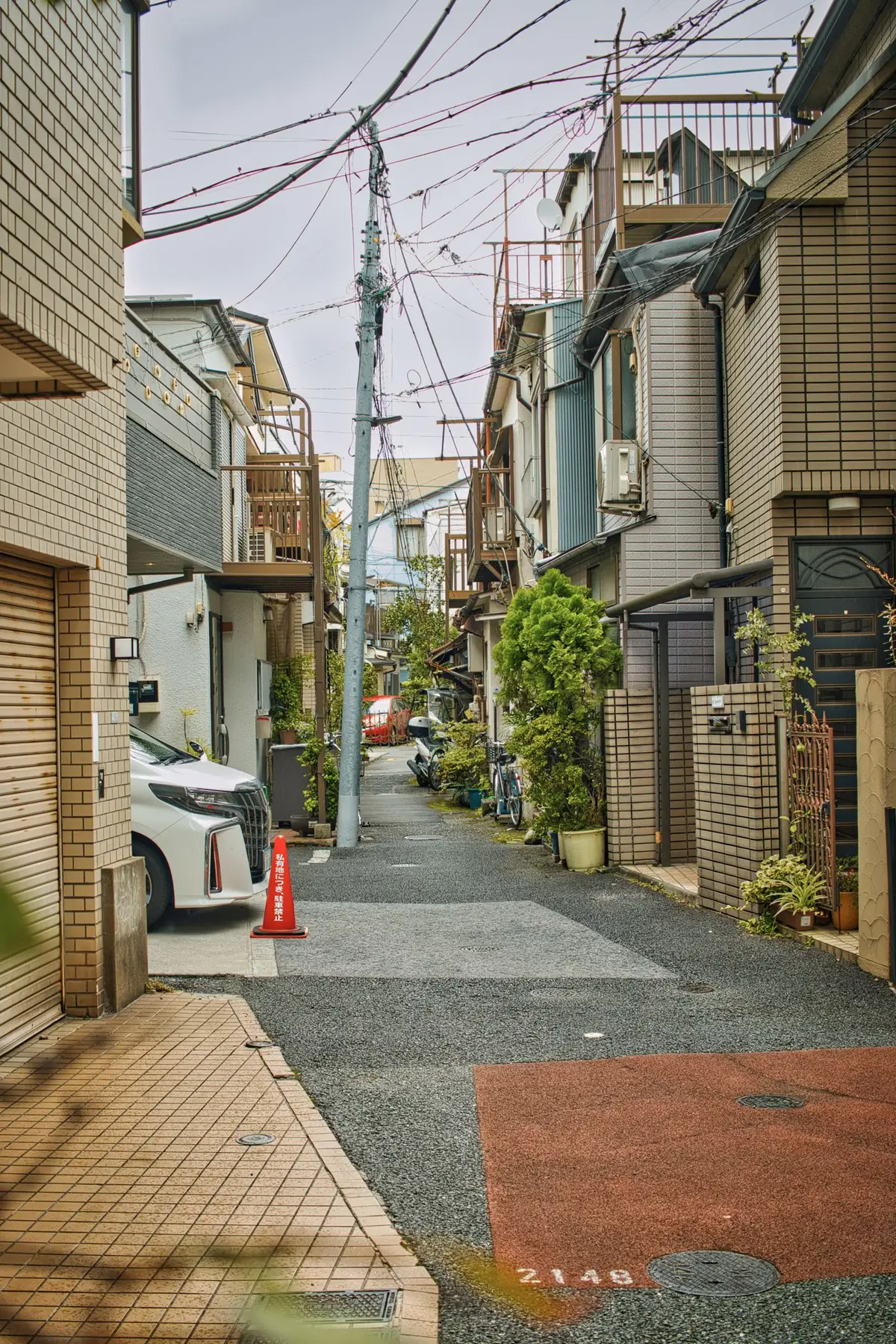 日本の住宅街の細い路地。電線が交差し、両側に住宅が並ぶ