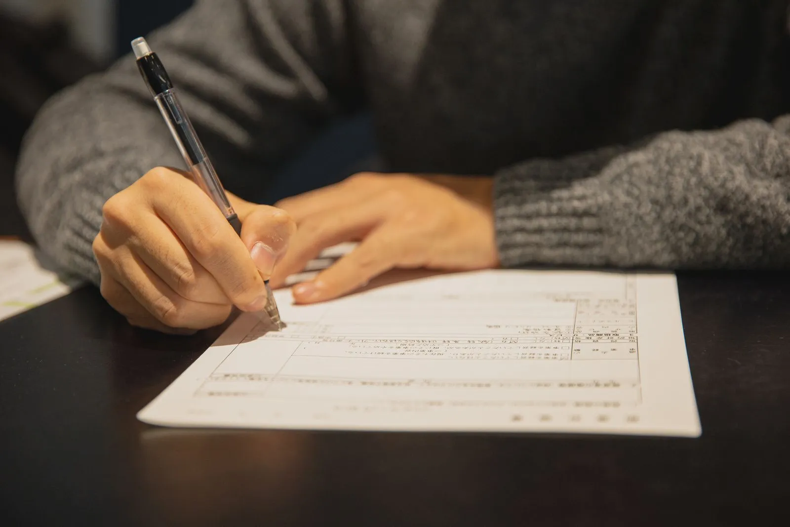 日本語の書式に手書きで記入している手元
