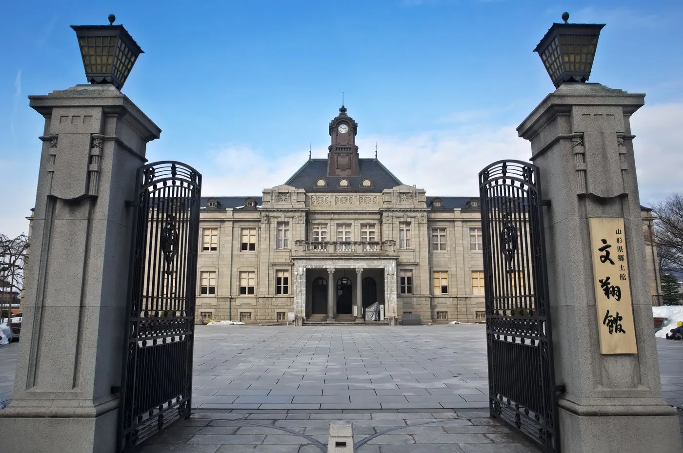 石造りの門柱と鉄扉の向こうに、時計塔をのせた石造りの洋風建築が建っている