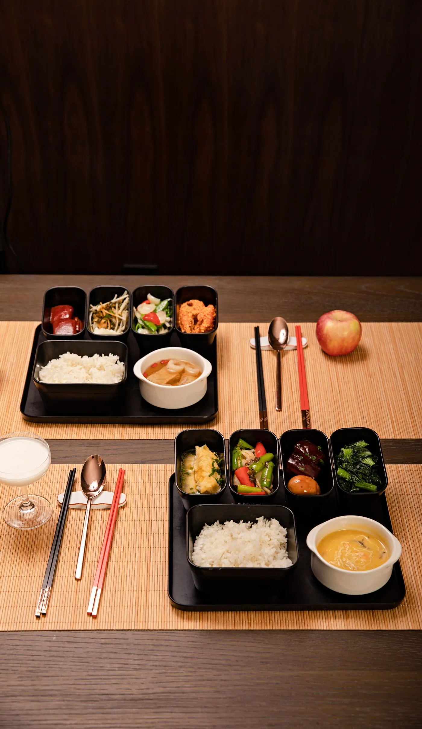 竹のランチョンマットの上に並べられた、ご飯・汁物・小鉢が載った黒い配膳トレー2人分