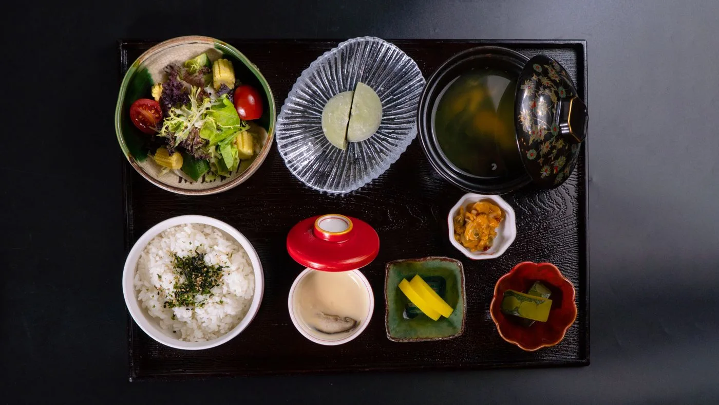 黒い盆に載せられた、ご飯・汁物・サラダ・小鉢が並ぶ和食の献立を真上から見たところ