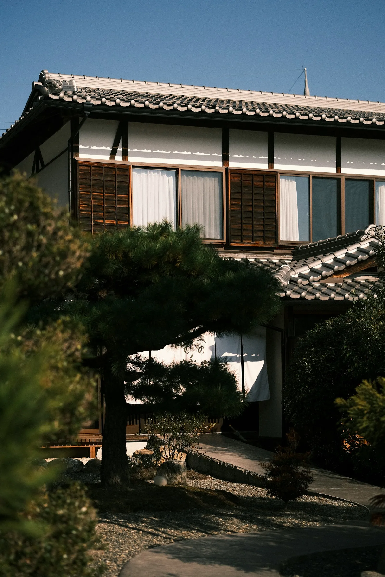 松の木のある庭と、瓦屋根に木製の雨戸を備えた日本家屋